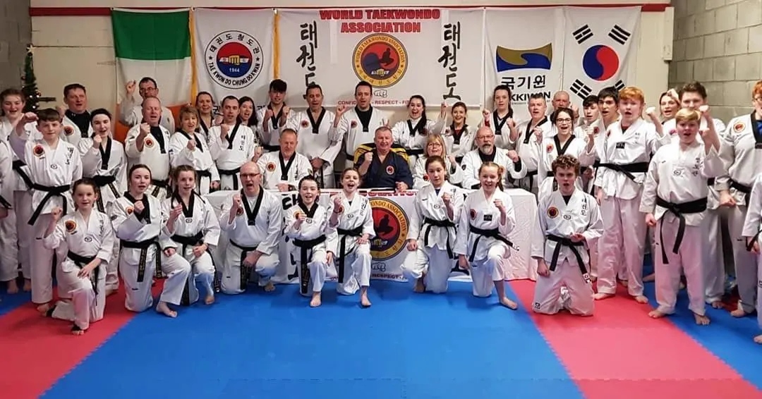 World Taekwondo Ireland black belts lined up in front of Irish, Korean and association flags