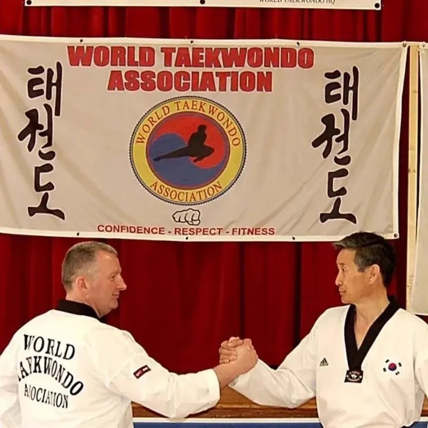 Grand Master Sheamus O'Neill and Grand Master Shin shaking hands under the World Taekwondo Association banner